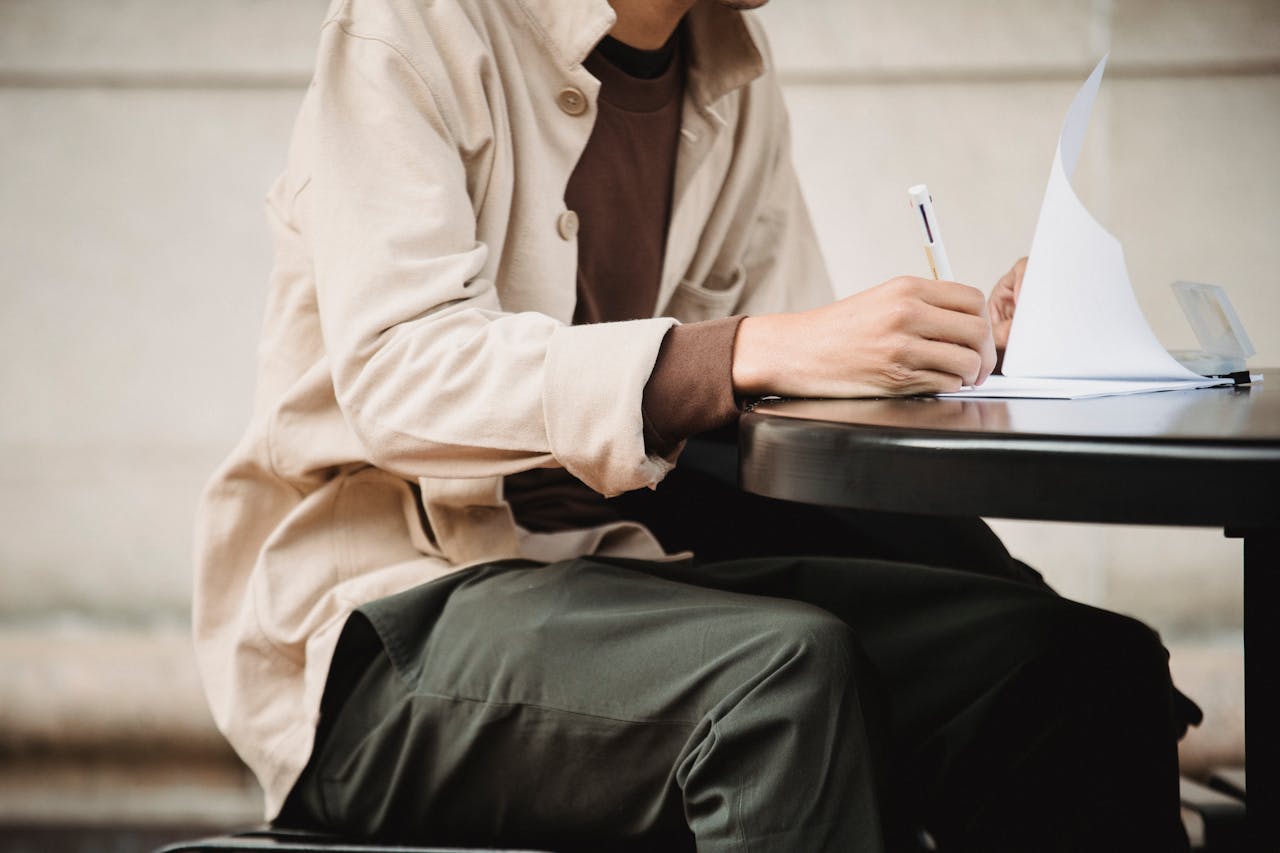 Side view of crop anonymous male learner writing in paper documents with pen while doing assignment